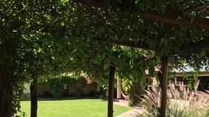 Un jardín con sendero de piedra, pérgola de madera y abundante vegetación.