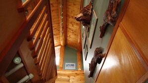 A wooden staircase with a handrail, leading to a room with wooden walls and a ceiling.