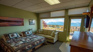 A bedroom with a bed, a sofa, a desk, and a window with a mountain view.