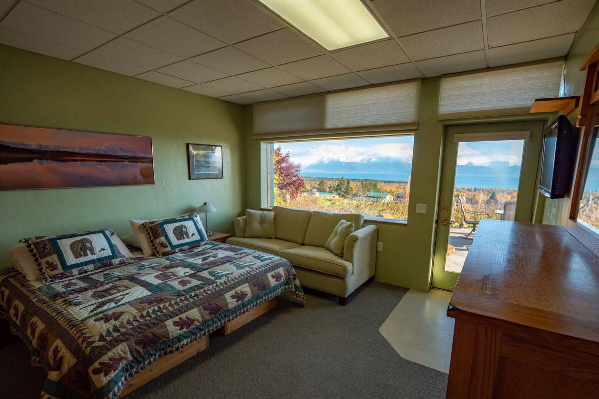 A bedroom with a bed, a sofa, a desk, and a window with a mountain view.