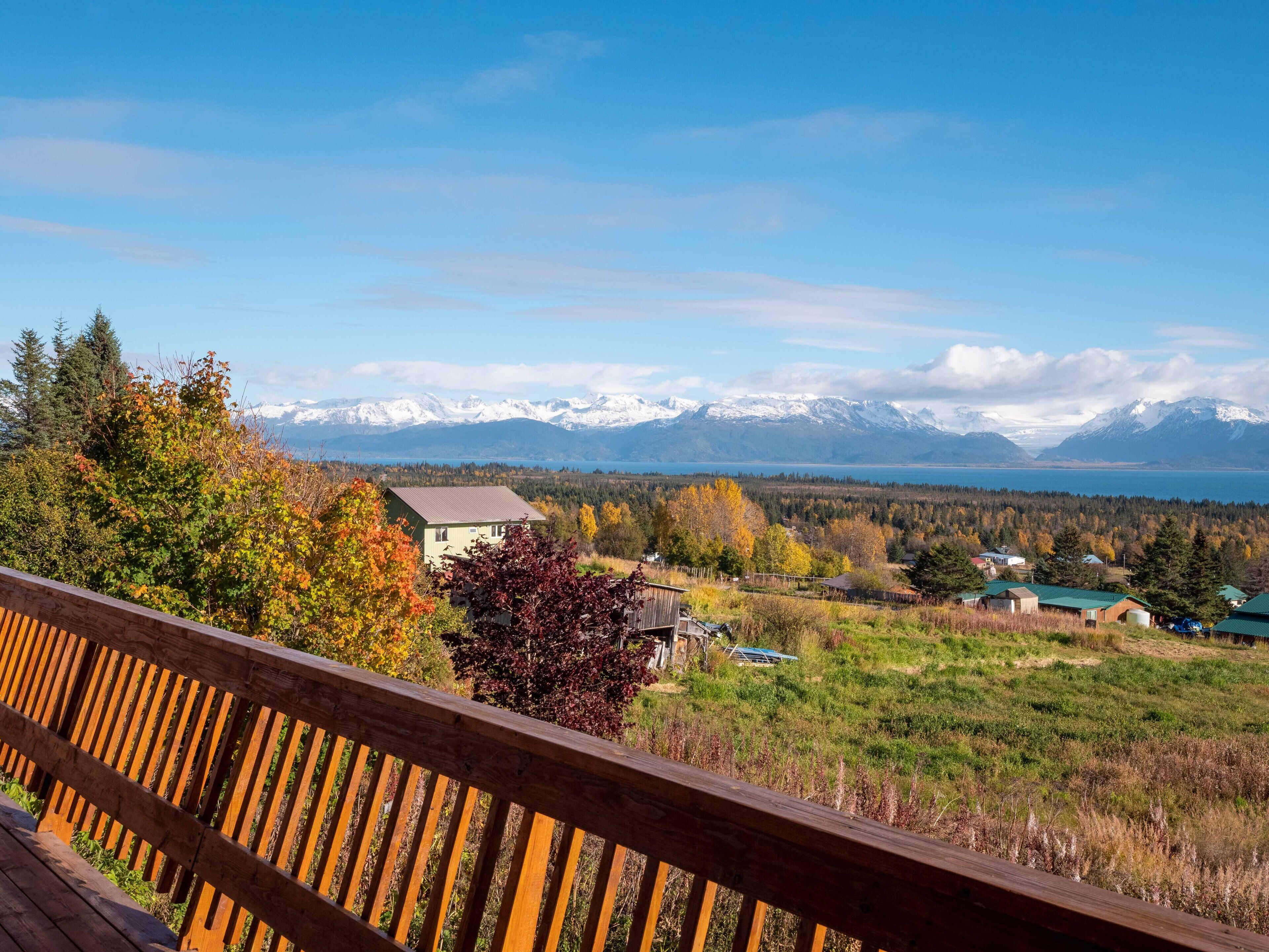A wooden deck overlooking a mountainous landscape with a lake and snow-capped peaks in the distance.