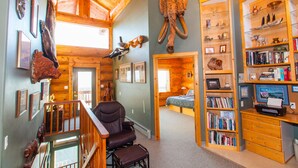A spacious room with a wooden ceiling, a large bookshelf, and a leather chair.