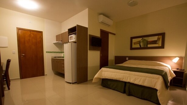 A hotel room with a bed, a desk, a refrigerator, a microwave, and a TV. - My Flat Hotel (Mogi das Cruzes)