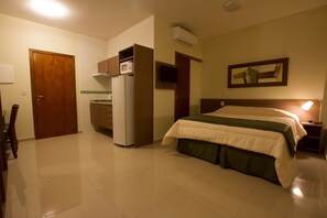 A hotel room with a bed, a desk, a refrigerator, a microwave, and a TV. - My Flat Hotel (Mogi das Cruzes)