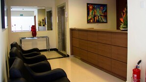 A reception area with a counter, a fire extinguisher, and a painting on the wall. - My Flat Hotel (Mogi das Cruzes)