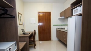 A compact kitchen with a refrigerator, microwave, and a small dining area with a table and chairs. - My Flat Hotel (Mogi das Cruzes)