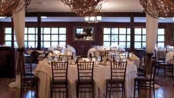 Un salón de banquetes con mesas redondas dispuestas para cenar, con manteles blancos y sillas de madera.