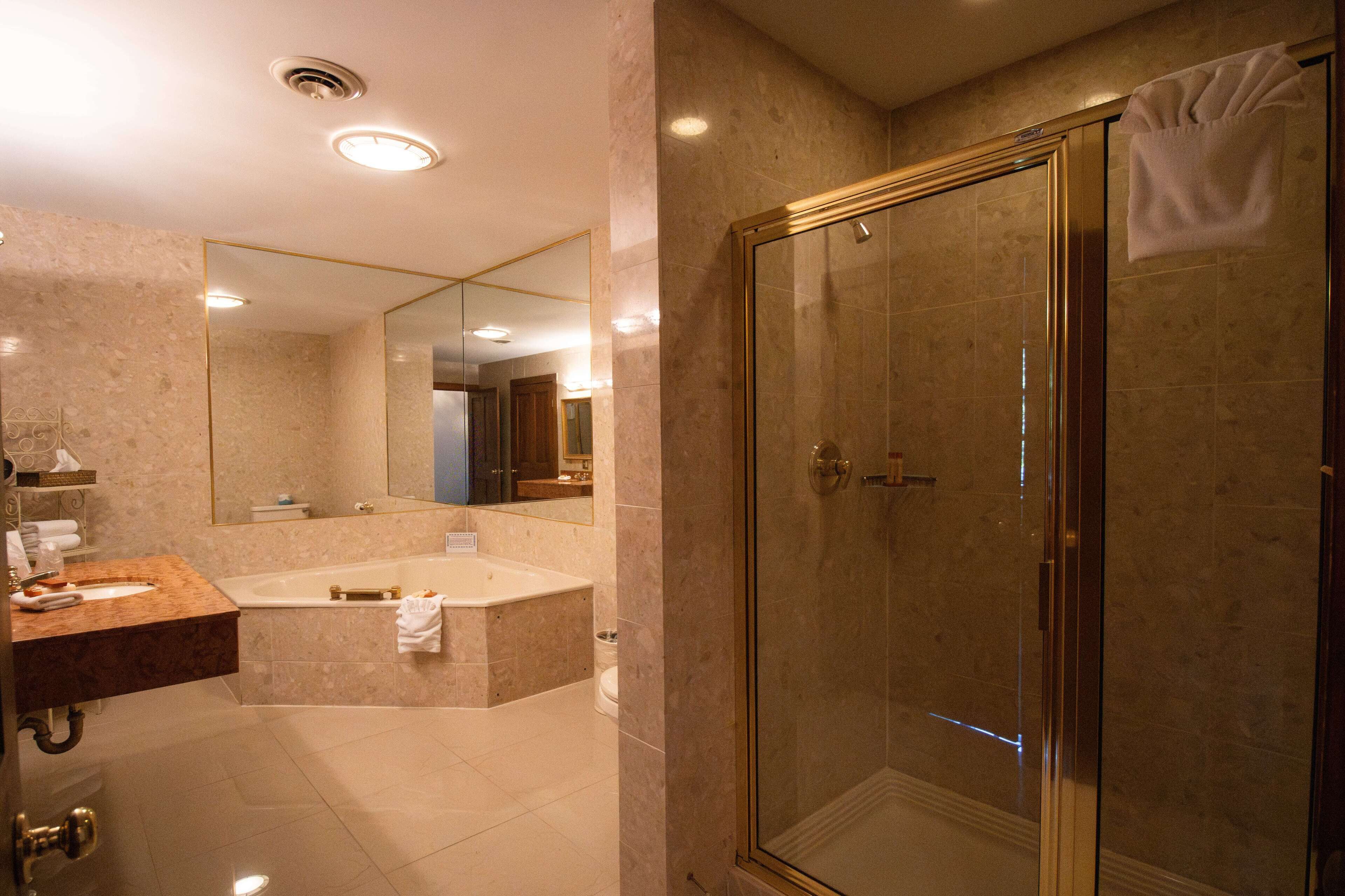Une salle de bain moderne dotée d’une douche à parois de verre, d’un grand miroir et d’un espace lavabo revêtu de carreaux de marbre.
