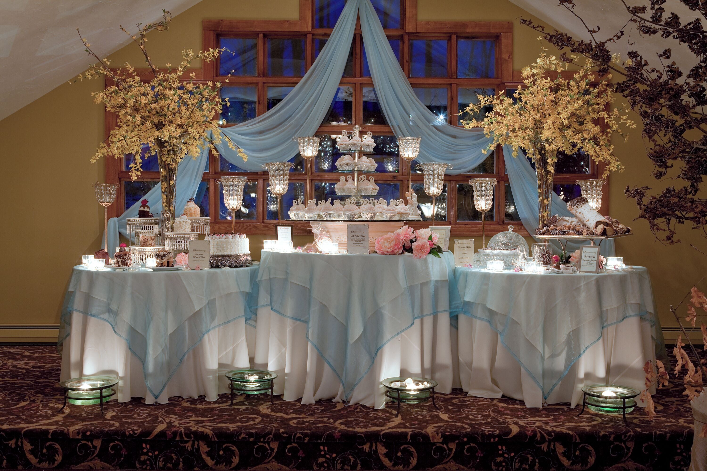 A banquet table set up with tiered cake stands and floral arrangements, draped with blue fabric.