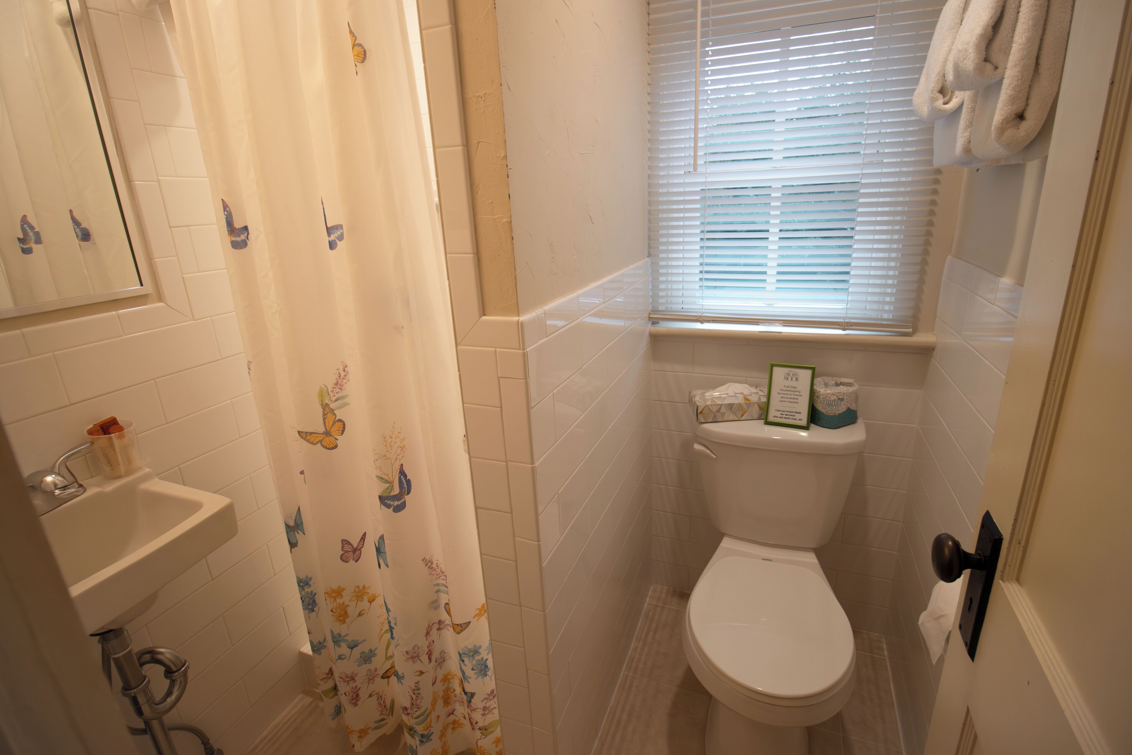 Et lille badeværelse med toilet, håndvask og bruseforhæng.