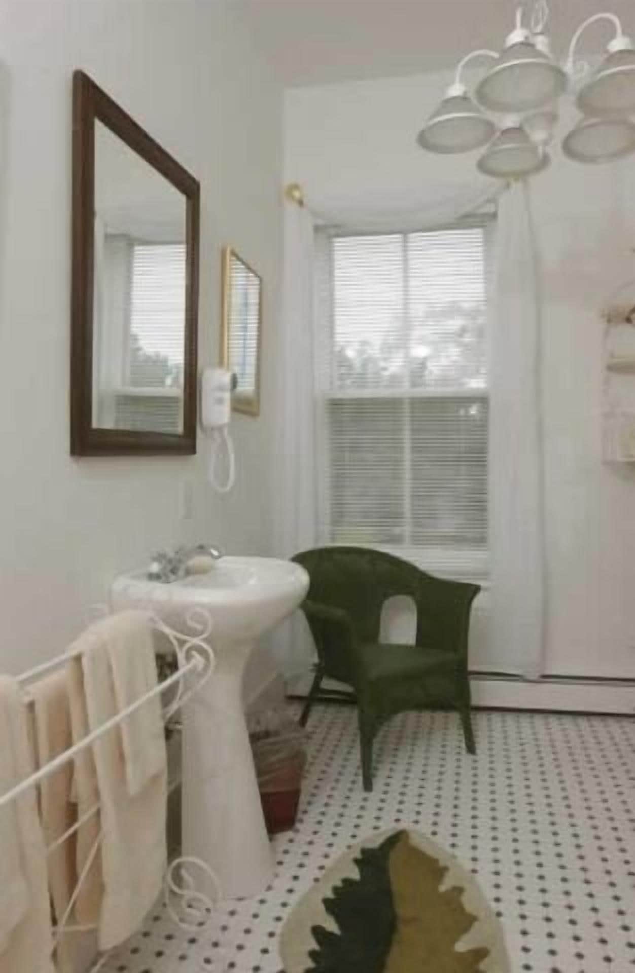 A bathroom with a white sink, a mirror, a green chair, and a patterned rug.