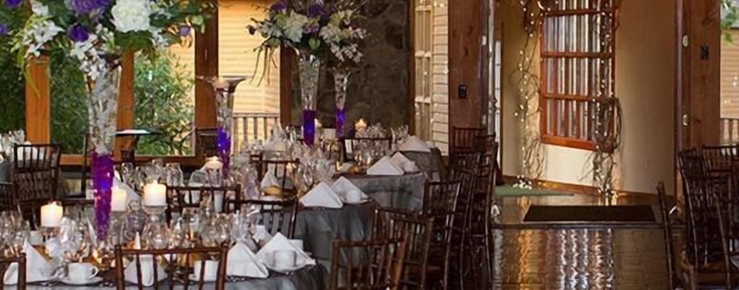 Une salle de banquet avec de nombreuses tables dressées pour un événement formel, agrémentée de compositions florales et d’un éclairage à la bougie.