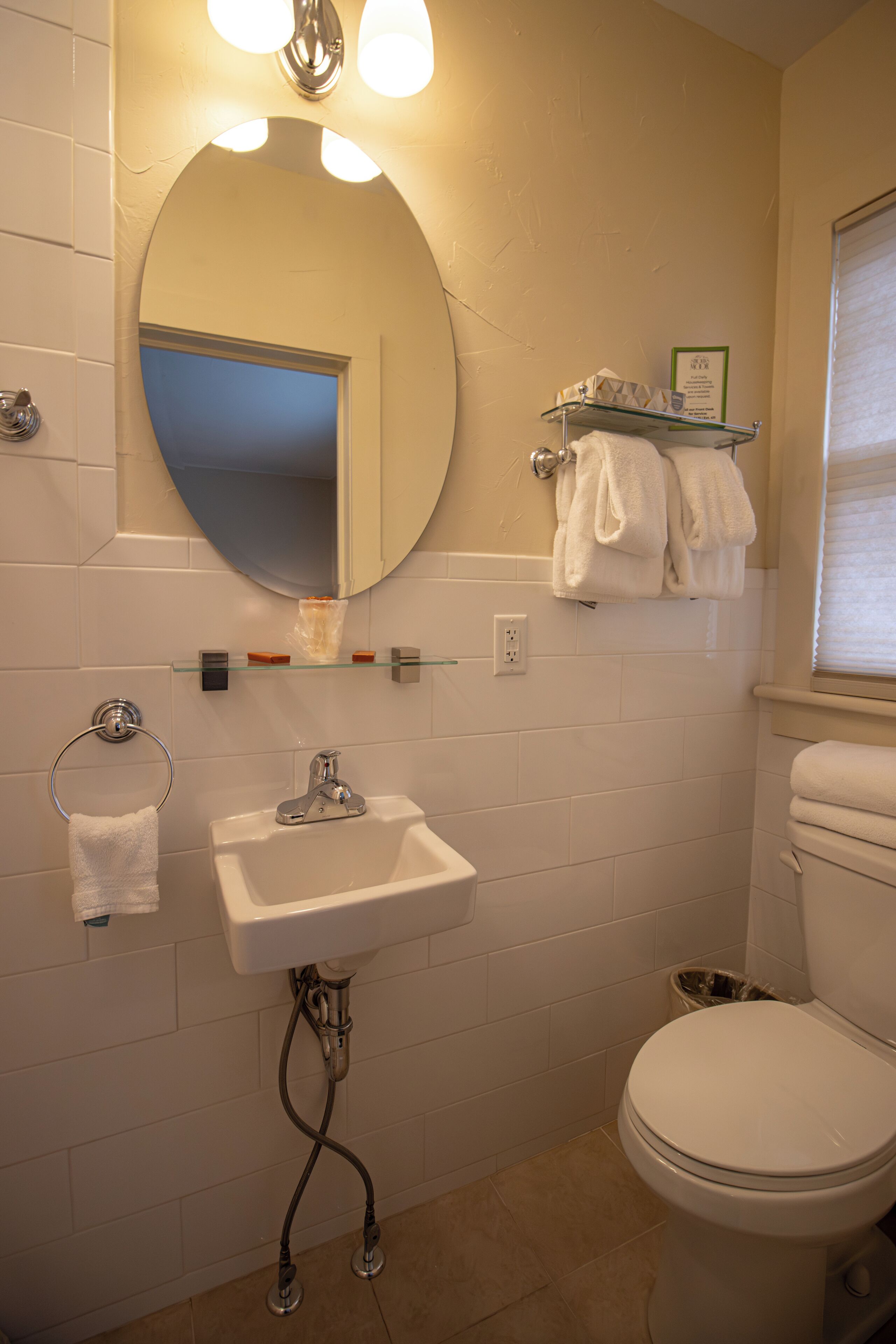 Une salle de bain avec un lavabo blanc, un miroir et des toilettes. Il y a des serviettes sur une étagère et une poubelle.