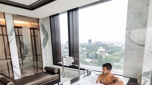 Een moderne badkamer met een groot bad vol bubbels, een bank en uitzicht op de stad.