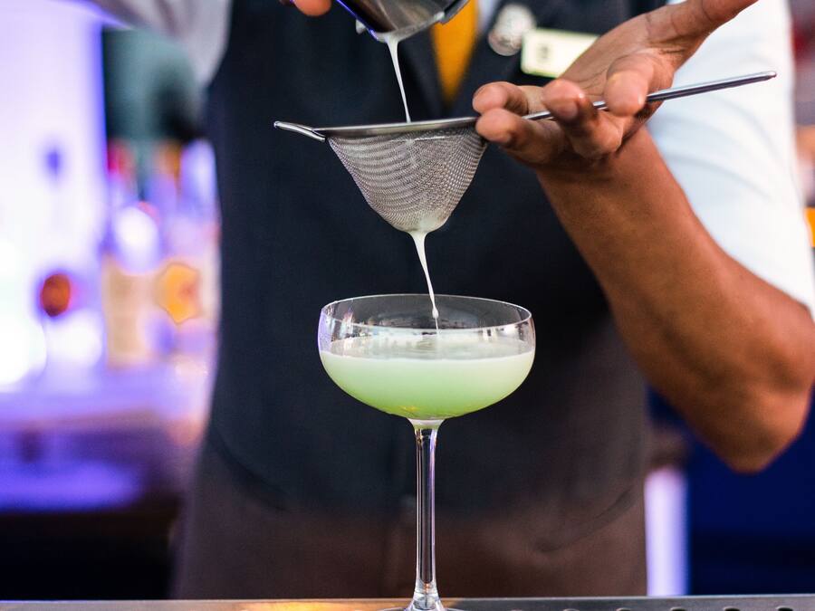 En bartender hælder en drink i et martiniglas med en si.