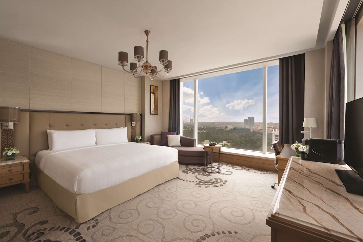 A hotel room with a large bed, a desk, a TV, and a view of the city.
