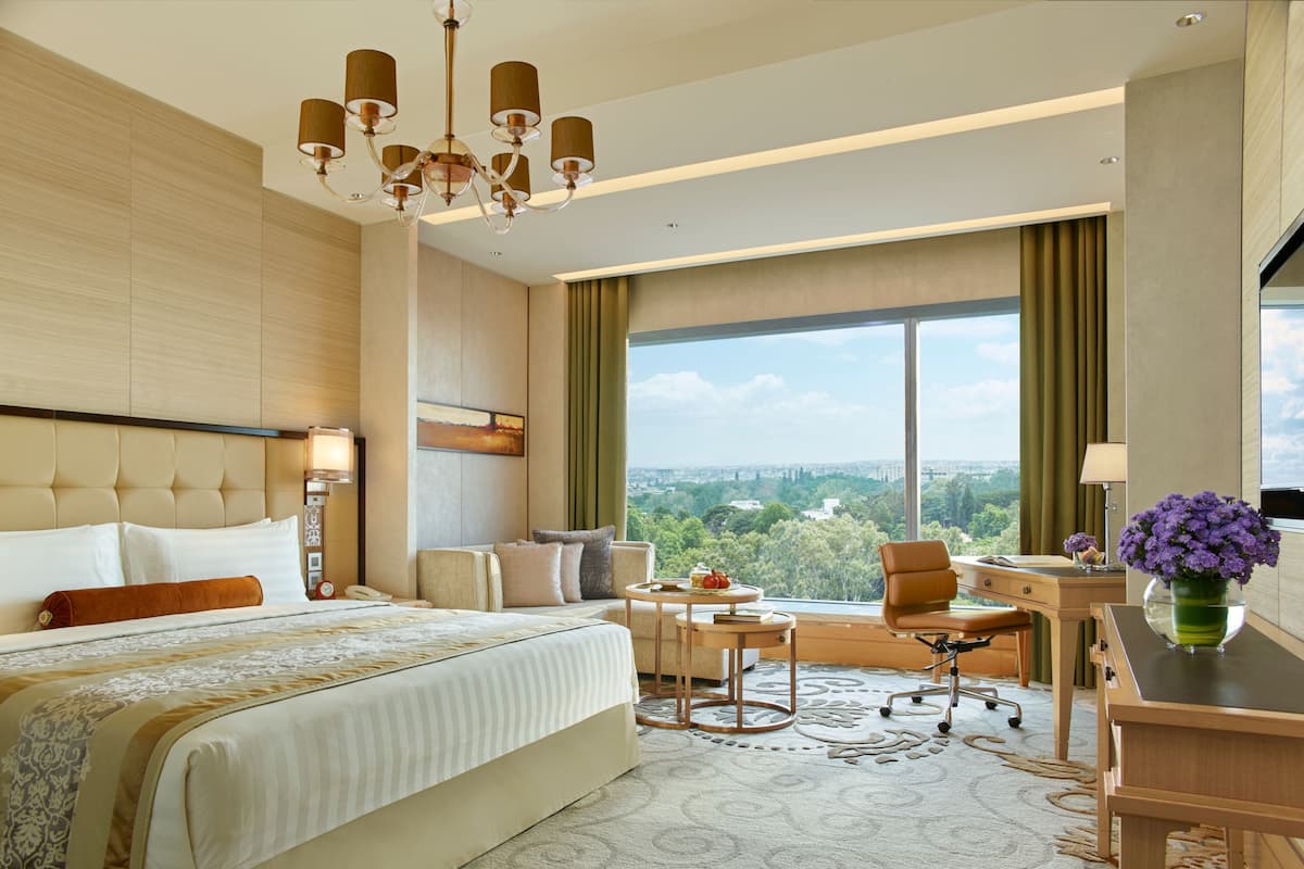 A modern hotel room with a large bed, a desk, a chair, and a view of the city.