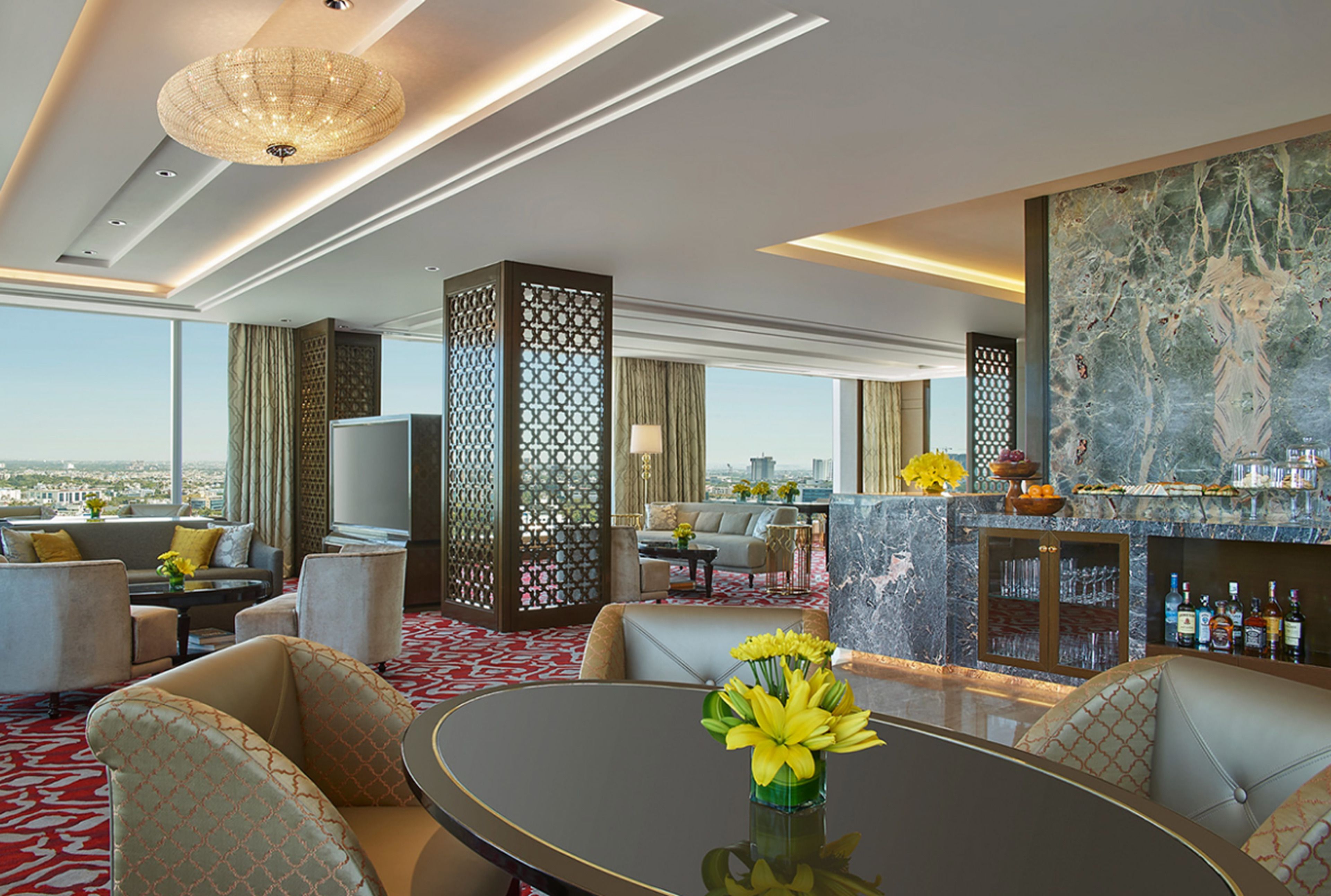 En modern hotellobby med ett runt bord, soffor, en bardisk och ett stort fönster med utsikt över staden.