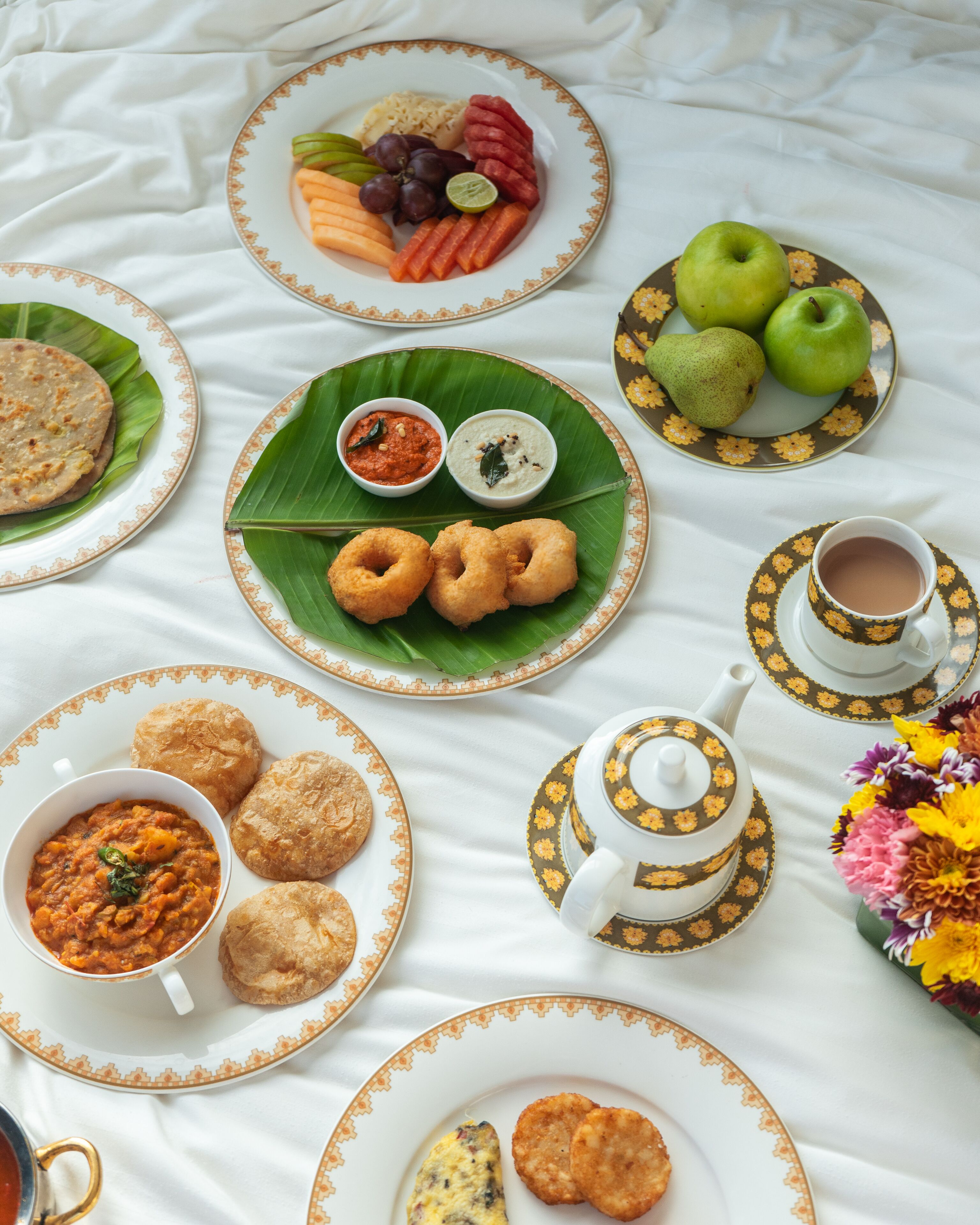 Mesa posta com diversos pratos, incluindo pães achatados, caril e petiscos, dispostos sobre um tecido branco.