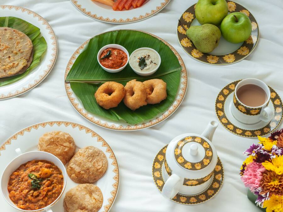 Mesa posta com diversos pratos, incluindo pães achatados, caril e petiscos, dispostos sobre um tecido branco.