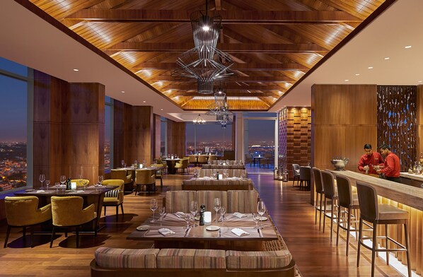 A modern restaurant with high ceilings, wooden paneling, and a city view. - Shangri-La Bengaluru (Bengaluru)