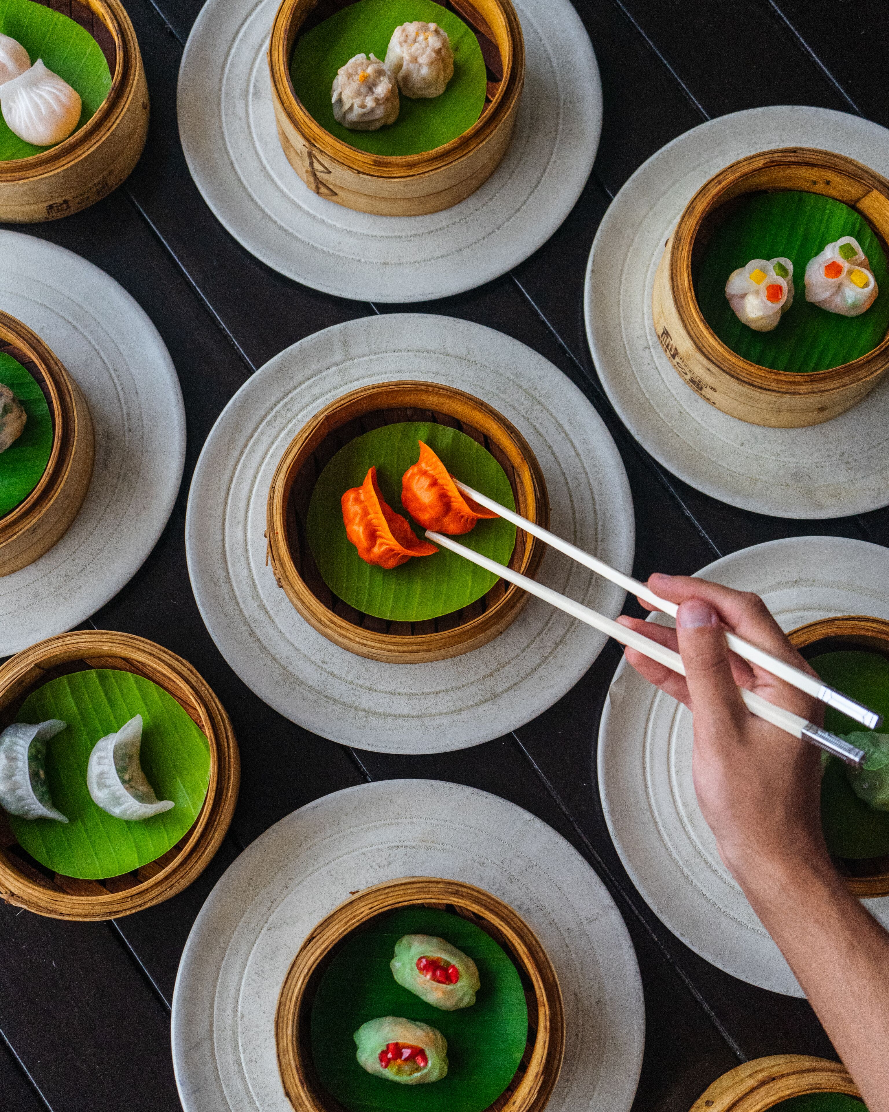 Verschiedene Dim-Sum-Gerichte auf Tellern und in Bambus-Dampfkörben angerichtet.