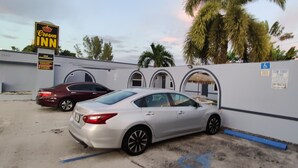 A parking area with a Crown Inn sign, a white wall with arched windows, and a palm tree in the background. - Crown Inn (Fort Lauderdale)
