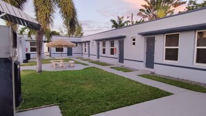 A courtyard with a thatched umbrella table, a small garden, and a building with numbered doors. - Crown Inn (Fort Lauderdale)