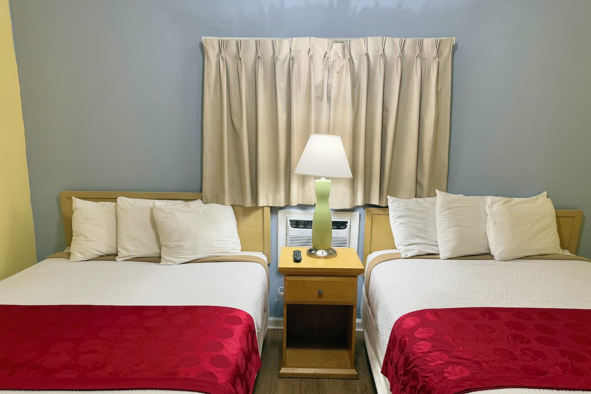 A hotel room with two beds, a nightstand with a lamp, and a window with curtains.