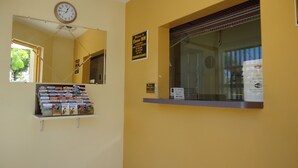 A reception area with a clock, a bulletin board with brochures, a window with a sign, and a wall-mounted sign. - Crown Inn (Fort Lauderdale)