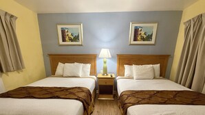 A hotel room with two beds, a nightstand with a lamp, and two framed pictures on the wall. - Crown Inn (Fort Lauderdale)