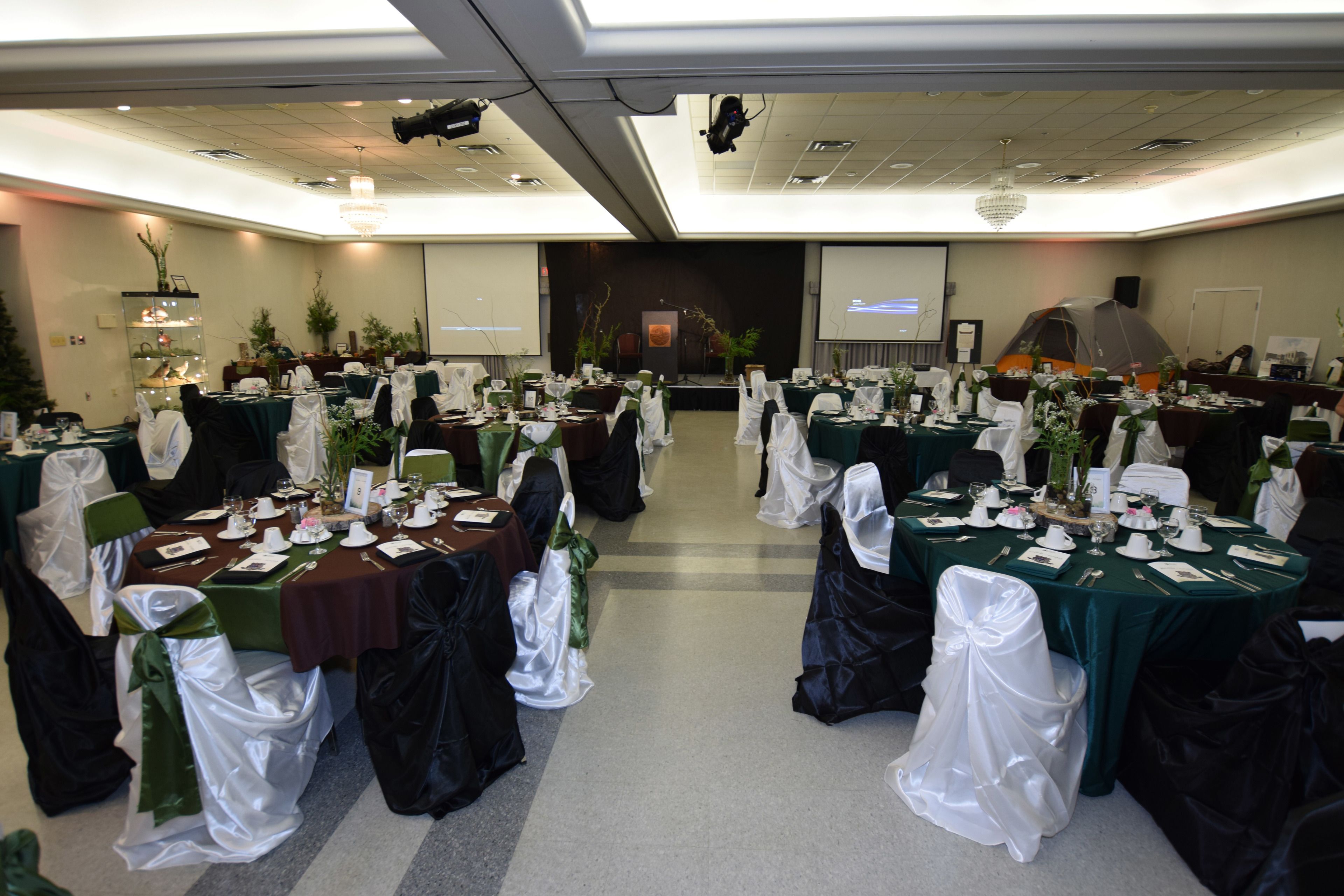 A banquet hall with multiple round tables set for a formal event, each with white tablecloths and green chairs.