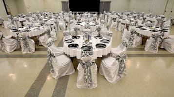 A banquet hall with round tables set for a formal event, featuring white tablecloths and black and white chair covers.