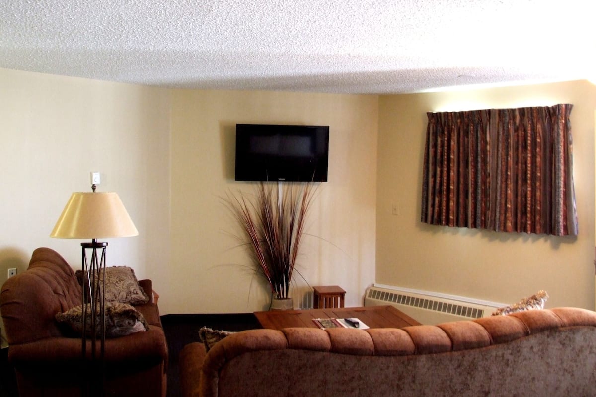 A living room with a sofa, a coffee table, a lamp, a TV, and a window with curtains.