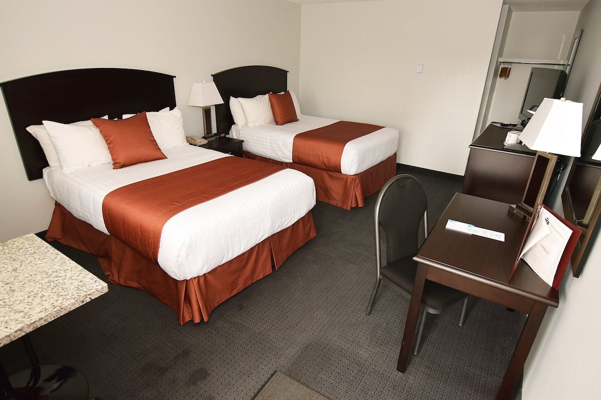 A hotel room with two beds, a desk, a chair, a lamp, and a mirror.