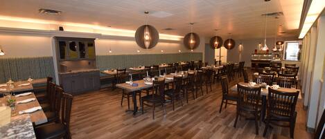 A restaurant with wooden flooring, multiple dining tables, and hanging pendant lights.