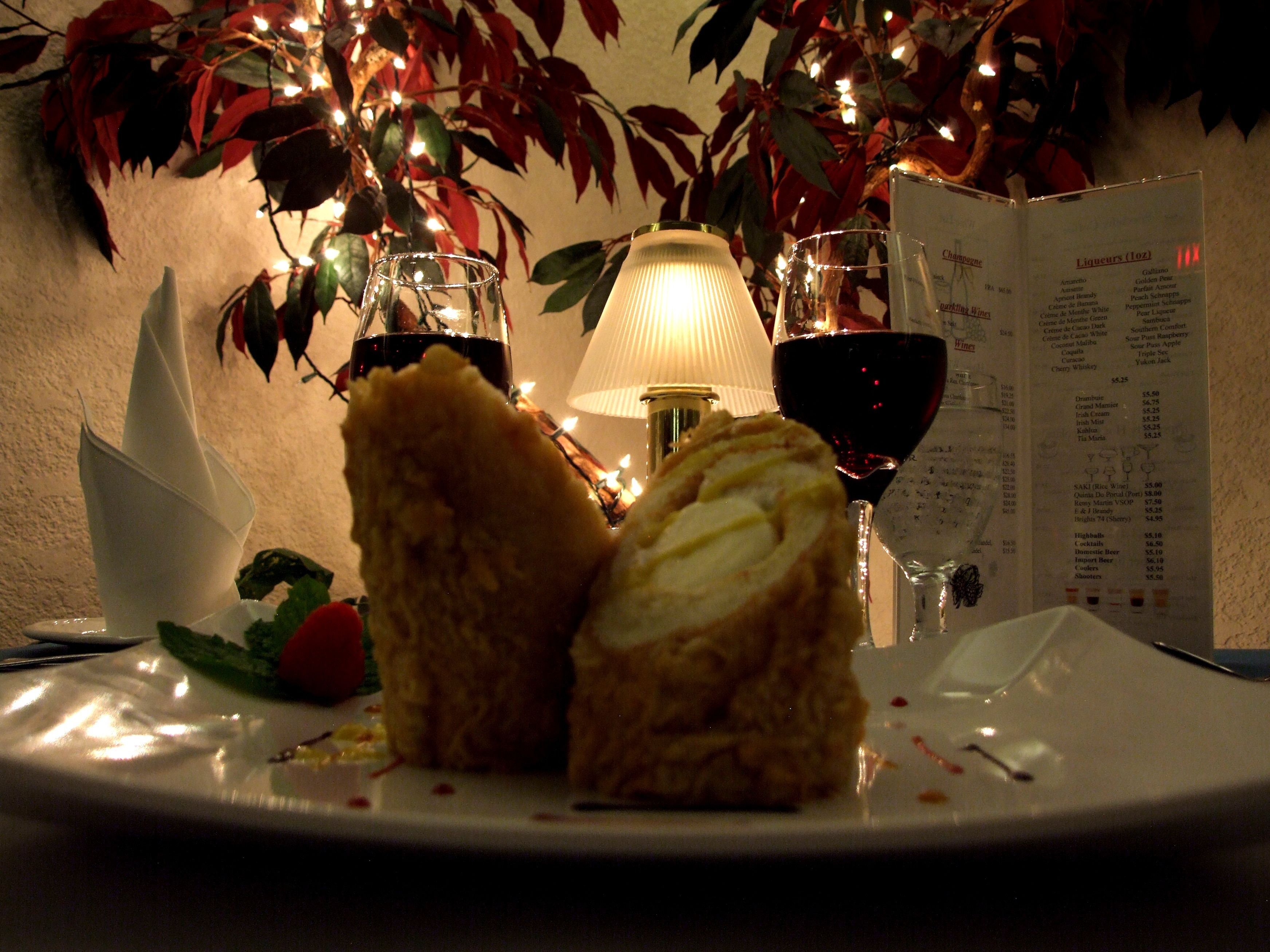 A plate with a sandwich and two glasses of red wine, a menu, and a lamp in the background.