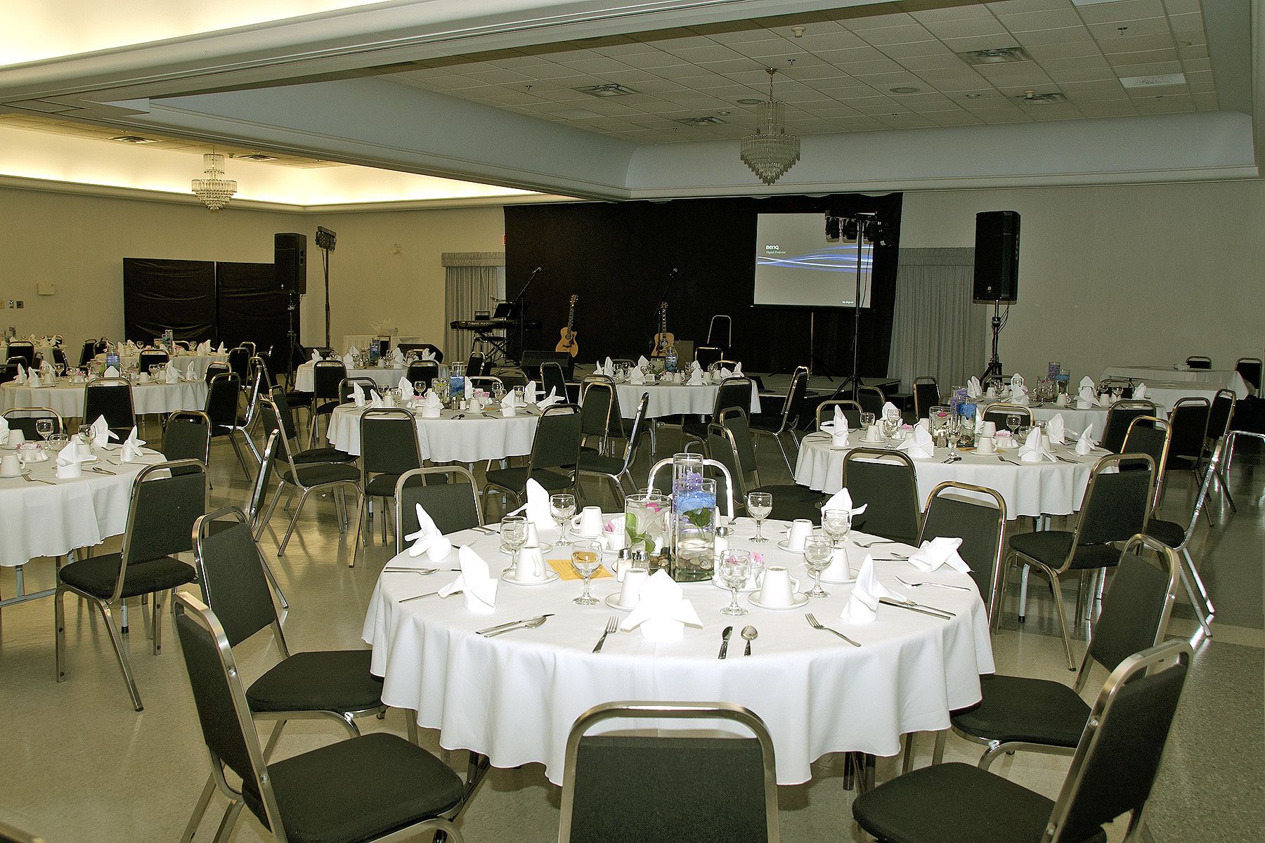 A banquet hall with round tables set for dining, equipped with chairs, tablecloths, and dining utensils.