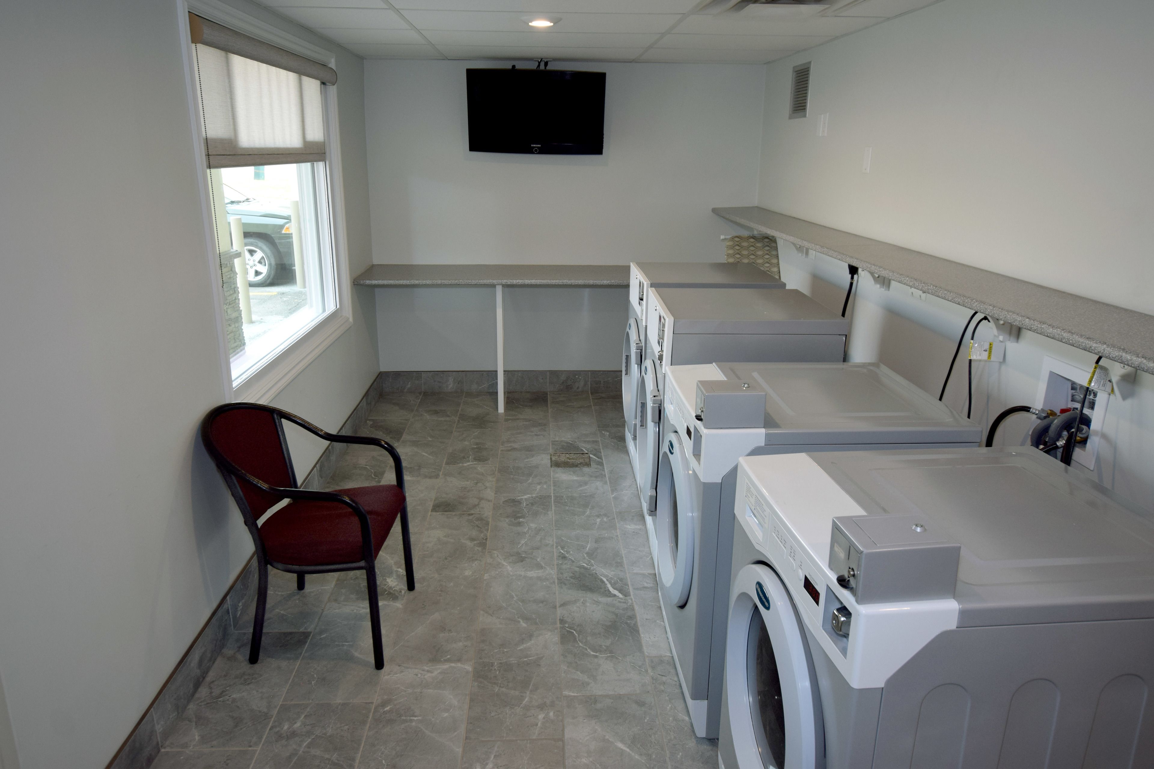 A laundry room with a washing machine, dryer, and a chair.