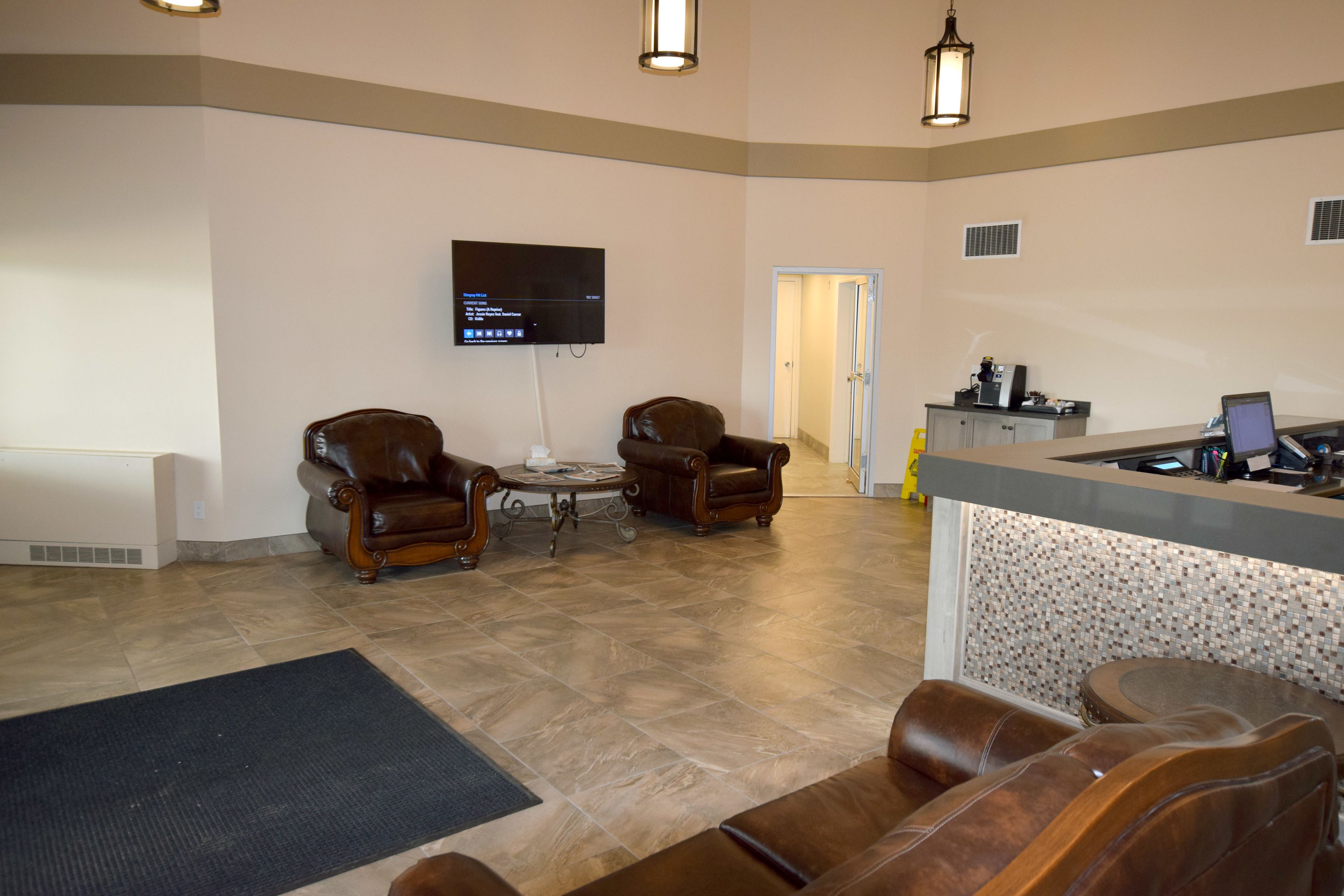 A spacious lobby with leather sofas, a reception desk, a flat-screen TV, and a tiled floor.