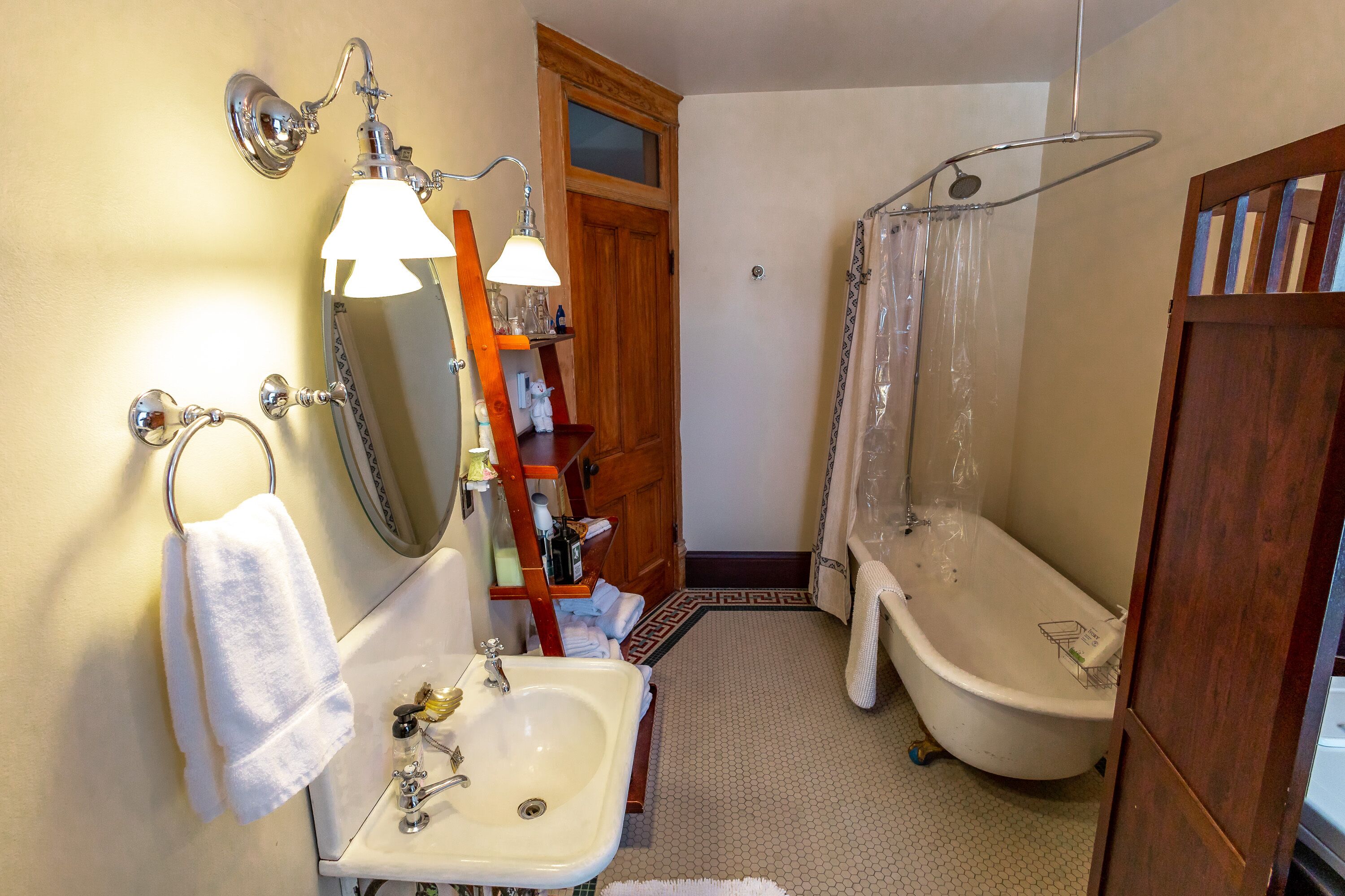 A bathroom with a sink, mirror, towel rack, shower, and wooden door.