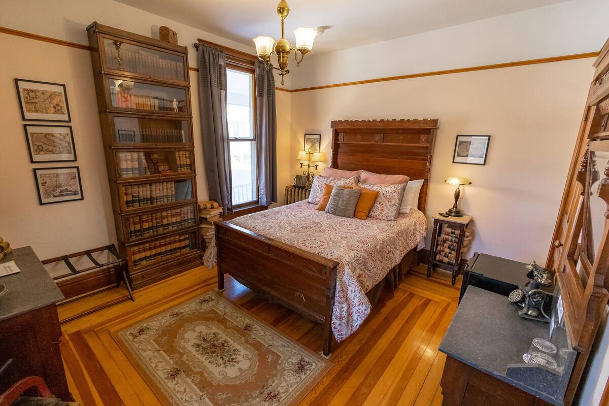Une chambre à coucher de style traditionnel, avec un lit en bois, une bibliothèque intégrée, un tapis à motifs et un petit bureau avec une lampe.
