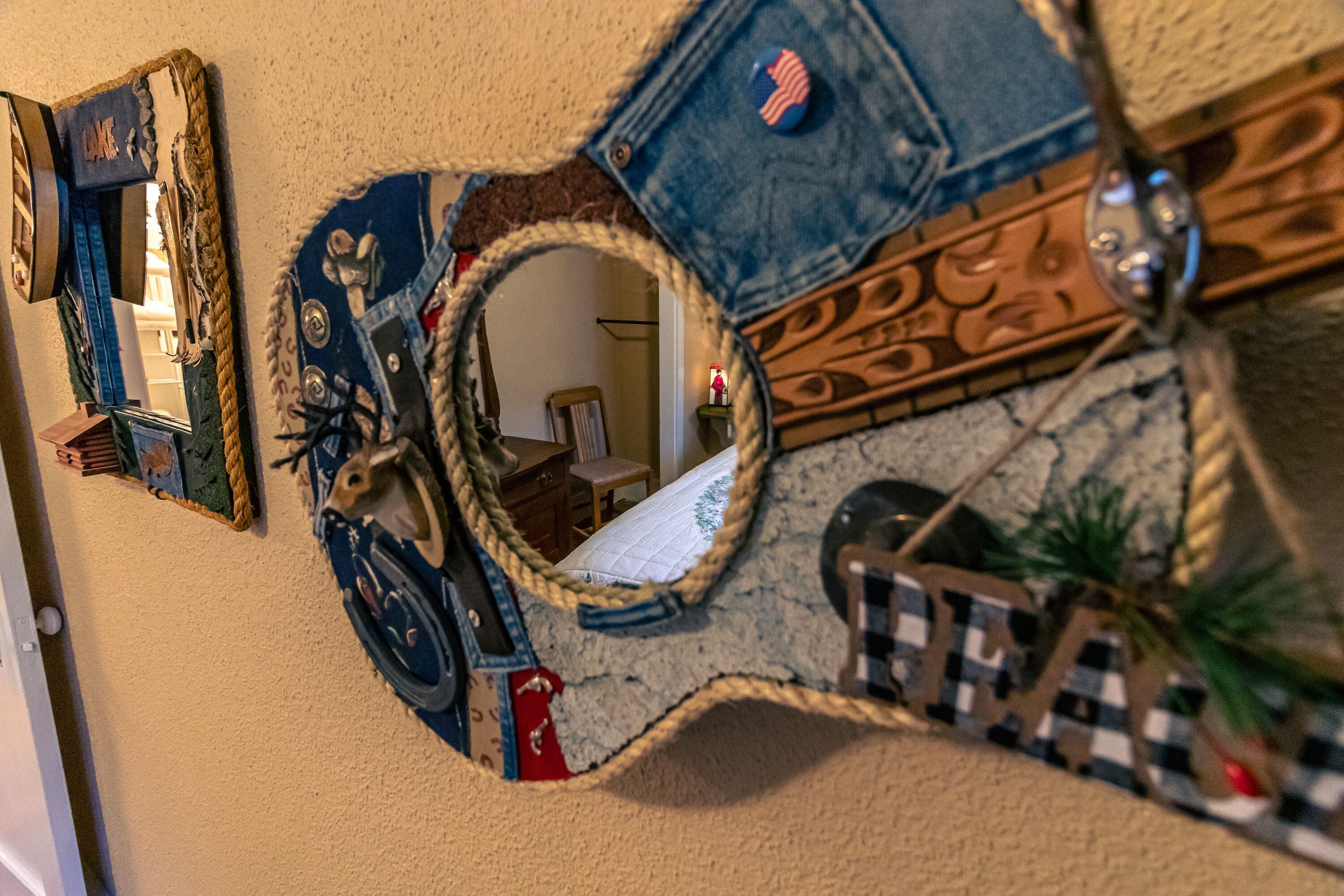 Een muur met een spiegel en decoratieve objecten, waaronder een denim patch, een klein Amerikaans vlaggenpinnetje en een geruit patroon.