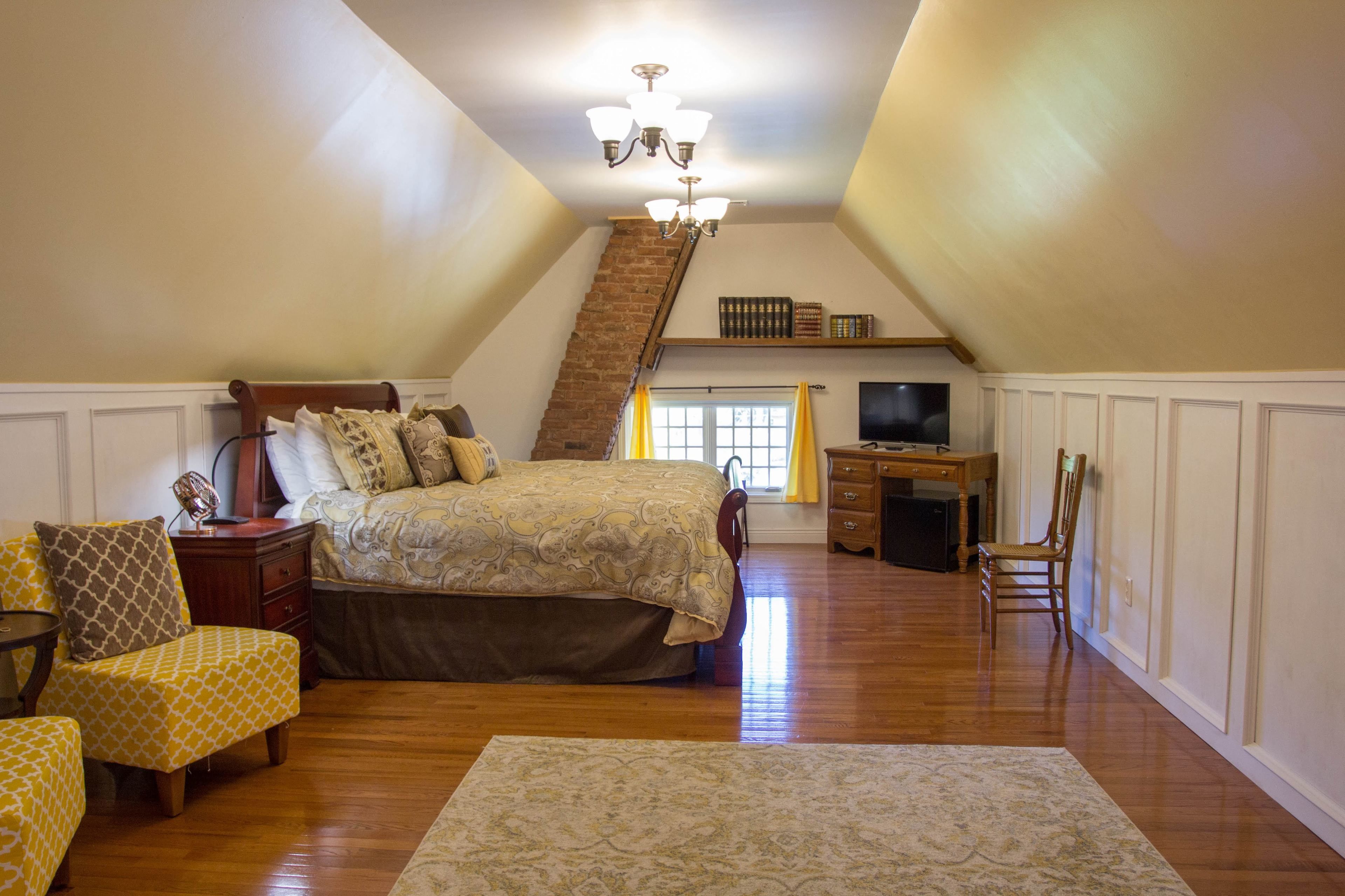A bedroom with a large bed, a desk, a chair, and a staircase leading to an upper level.