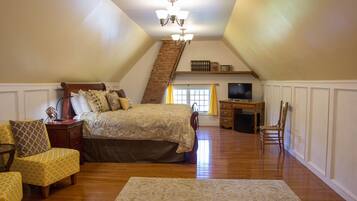 A bedroom with a large bed, a desk, a chair, and a staircase leading to an upper level.