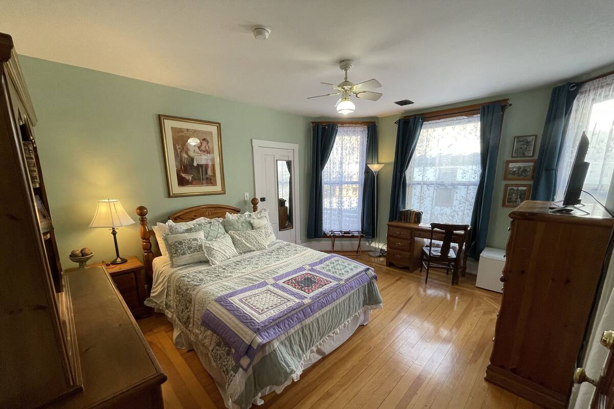 Une chambre à coucher comprenant un lit, un bureau, une chaise, une commode et un ventilateur de plafond.