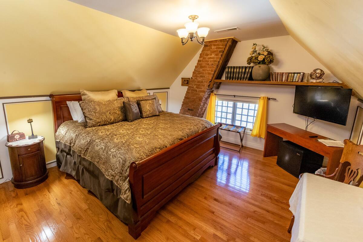 Une chambre à coucher avec un lit en bois, une table de chevet, un bureau, une télévision et une bibliothèque.