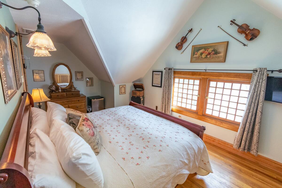 Une chambre à coucher avec un grand lit, une commode en bois, un miroir et une fenêtre avec des rideaux.