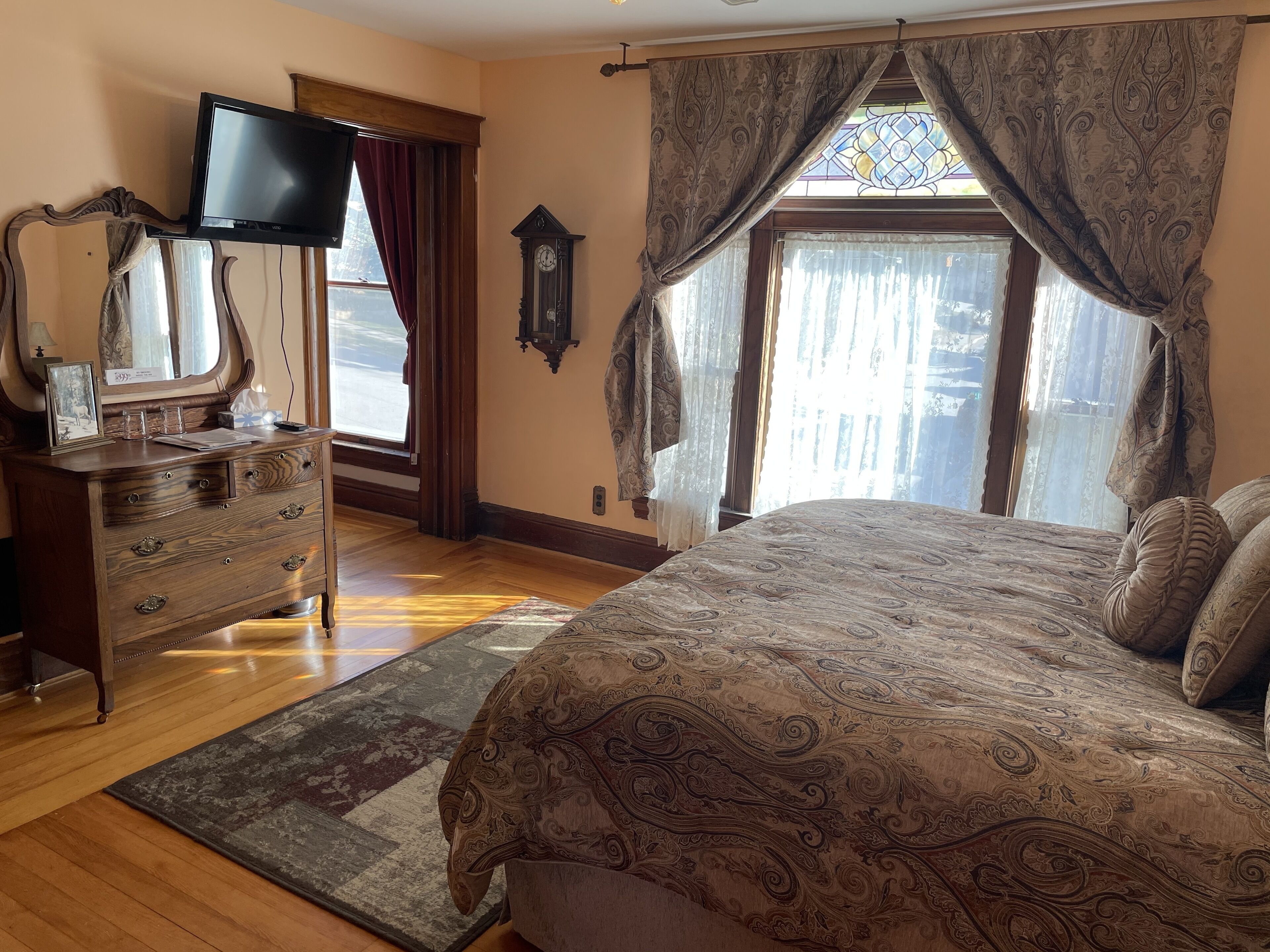 Un dormitorio con una cama grande, un aparador, un televisor de pantalla plana, un reloj y una ventana con cortinas.