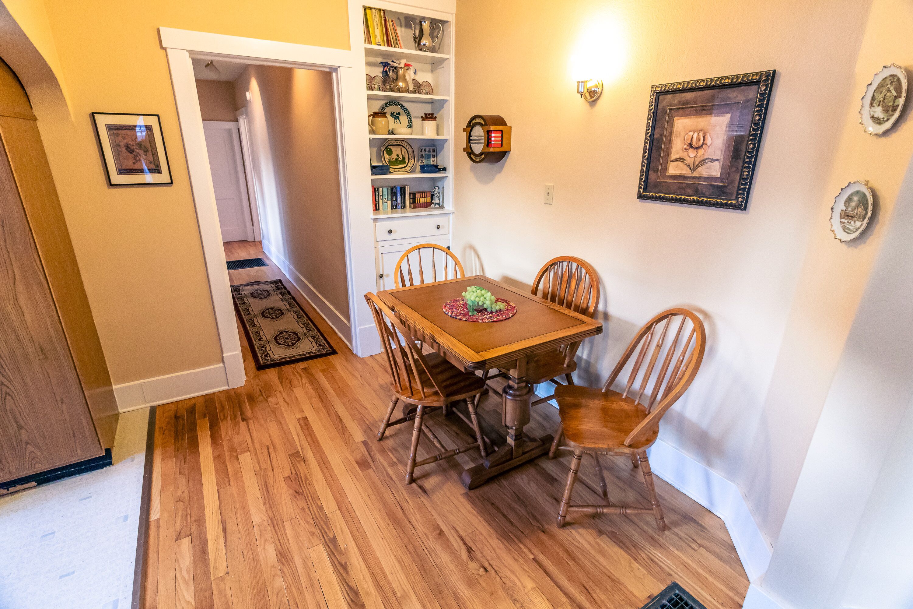A dining area with a wooden table and chairs, a bookshelf, and a framed picture on the wall.